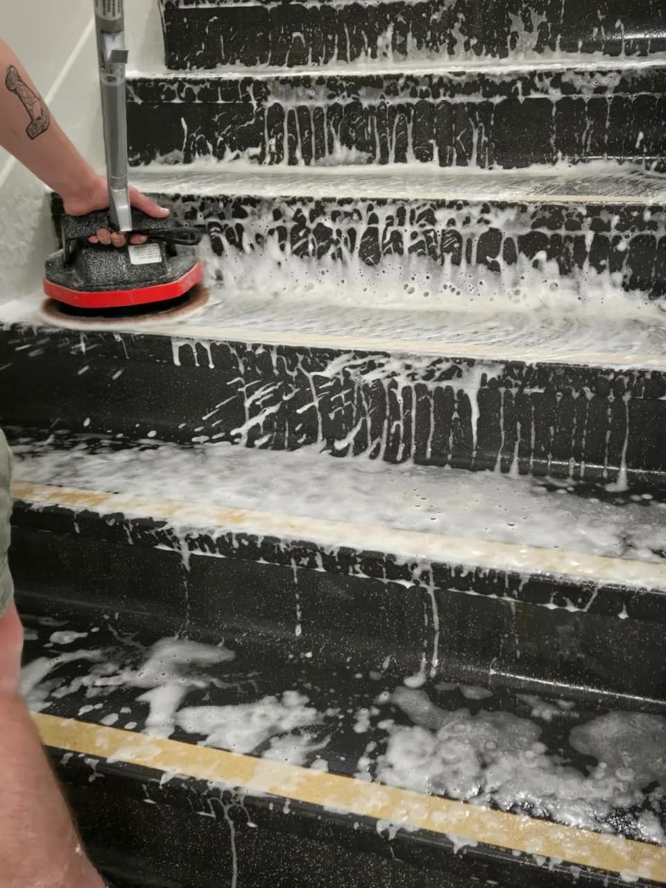 Technician using a handheld scrubber on hard stair treads covered in cleaning foam
